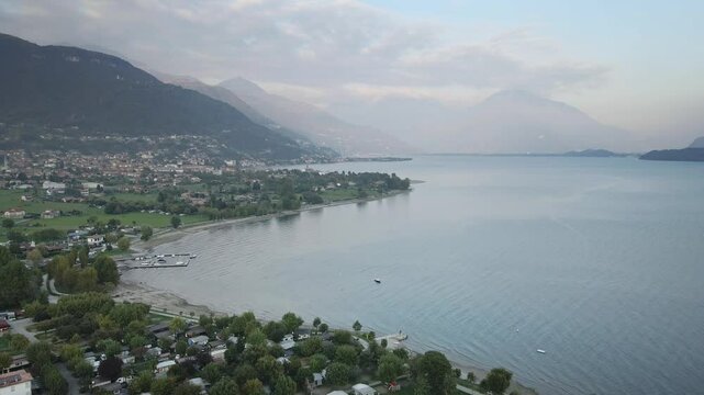 A stunning drone shot of the Italian lake town Dongo in Lake Como, flying over the town with majestic mountains and the shimmering lake creating a breathtaking backdrop.