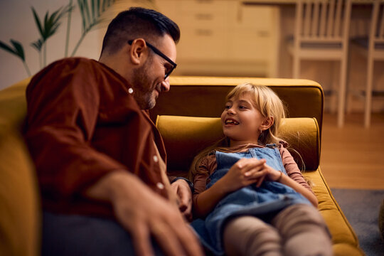 Happy little girl and her father communicating while relaxing on sofa.