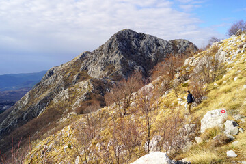A man walks along a marked tourist route in Orjen, Montenegro: landscape with the peak of Radostak and a tourist relaxing during the climb up the mountain. The person is engaged in active recreation.