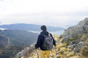 A man with a backpack, photographed from behind, descends a mountain path marked with red and white...