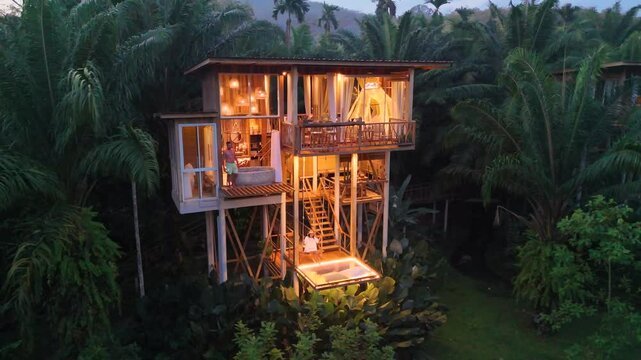 Nestled high in the trees, this enchanting retreat glows warmly as night falls. Surrounded by vibrant foliage, it offers a serene escape into nature beauty under a starlit sky. tree house in jungle