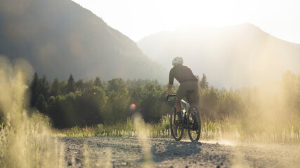 Gravel biker on a dirt path during golden hour in a calm valley.