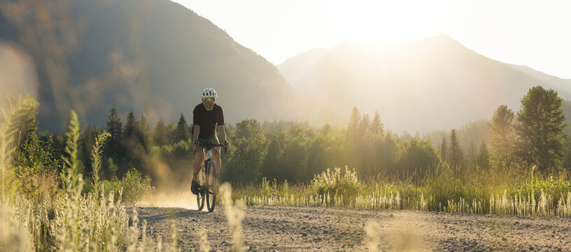 Cyclist pedaling a dirt road framed by fields and distant mountains.