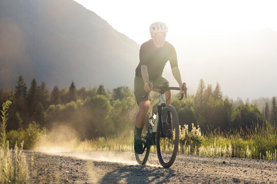 Cyclist on a gravel road in a sunlit rural landscape by mountains.