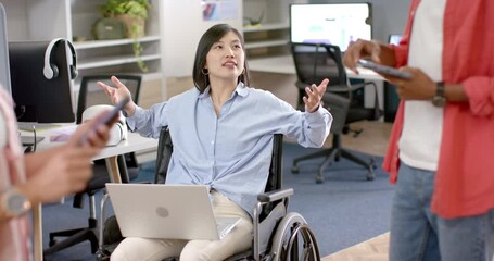Discussing ideas, woman in wheelchair with laptop engaging with colleagues in office