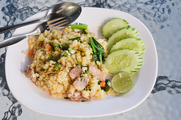 plate of fried rice (Khao Pad) served with slices of cucumber and a wedge of lime on the side.The fried rice contains pieces of meat,likely pork,along with vegetables such as carrots and green onions