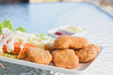 plate of food placed on a glass table.The plate contains several golden-brown fried chicken nuggets,alongside a side of fresh salad consisting of lettuce,and cabbage drizzled with a white dressing.