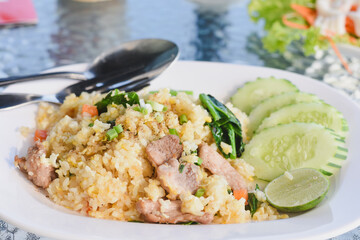 plate of fried rice (Khao Pad) served with slices of cucumber and a wedge of lime on the side.The fried rice contains pieces of meat,likely pork,along with vegetables such as carrots and green onions