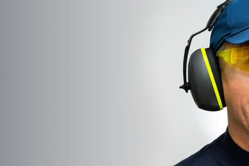 A man wearing  headphone against grey wall with place for text. Noise protection concept.