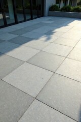 Fototapeta premium Sunlit Patio with Large Square Paving Stones and Modern Building in Background