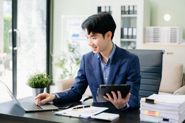 Obraz premium Young business man working at office with laptop, tablet and taking notes