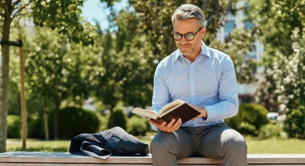 Fototapeta premium Middle-aged man with gray hair reading book outdoors