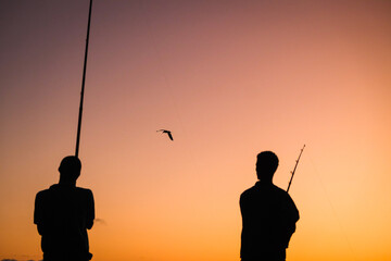 Silhouette photo of two anglers against orange sky
