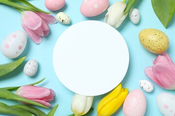 Colorful eggs with tulip flowers and white paper card for text on pastel blue backdrop, space for your text or advertisement