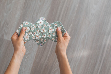 Reusable cloth menstrual pad with a floral pattern held by two hands on a wooden floor background concept of sustainability