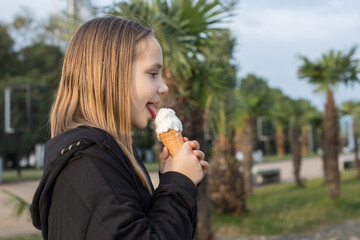 Happy young girl holds a vanilla ice-cream in cone and walking in park outdoors