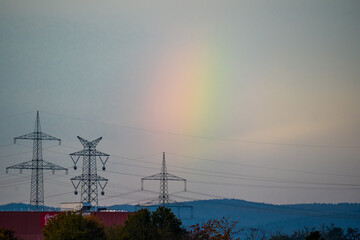 Multicolored short rainbow over hills, power lines in foreground