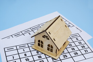 Wooden house model on 2 calendar pages on blue background. Room for text.