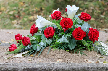 Flower arrangement on an urn grave. Red roses and white lilies in the cemetery. A beautiful bouquet of memorial flowers. Relatives have brought memorial flowers to the grave.

