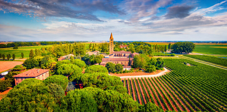 Colorful summer landscape of Pomposa Abbey tower among vineyards. Stunning morning view from flying drone of Italian countryside, Province of Ferrara, Italy. Beauty of countryside concept background..