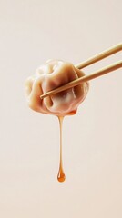 Delicious dumpling held by chopsticks with sauce dripping down in a minimalist setting