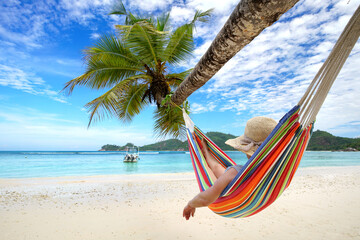 relaxing in vacation, woman on a colorful hammock on a tropical beach with palms and turquoise sea	
