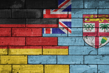 colourful painted big flag of germany and flag of Fiji on a massive old brick wall background....
