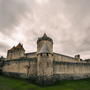 Vista de gran angular de la fachada del castillo medieval de piedra de Carcassonne con torres y murallas bajo un cielo nublado.