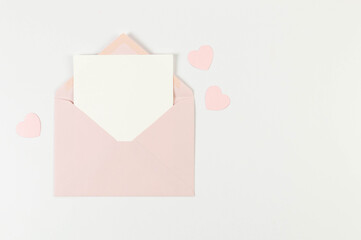 Top view of pink envelope, white card on white background. Valentine's day, pink hearts, love. Post flat lay, copy space.