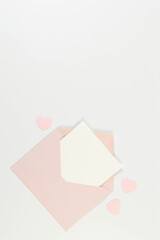 Top view of pink envelope, white card on white background. Valentine's day, pink hearts, love. Post flat lay, copy space.