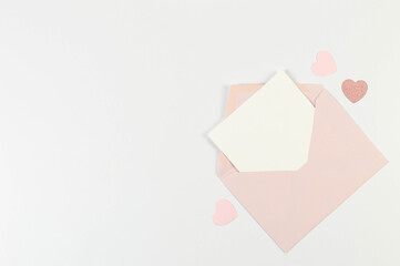 Top view of pink envelope, white card on white background. Valentine's day, pink hearts, pink glitter heart, love. Post flat lay, copy space.