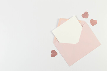 Top view of pink envelope, white card on white background. Valentine's day, pink glitter hearts, love. Post flat lay, copy space.