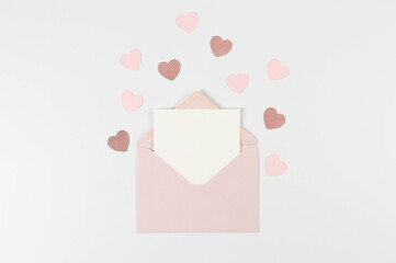 Top view of pink envelope, white card on white background. Valentine's day, pink hearts, pink glitter heart, love. Post flat lay, copy space.