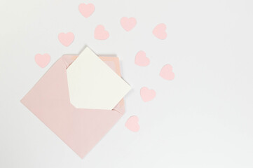 Top view of pink envelope, white card on white background. Valentine's day, pink hearts, love. Post flat lay, copy space.