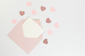 Top view of pink envelope, white card on white background. Valentine's day, pink hearts, pink glitter heart, love. Post flat lay, copy space.