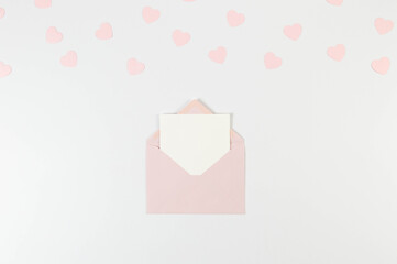 Top view of pink envelope, white card on white background. Valentine's day, pink hearts, love. Post flat lay, copy space.