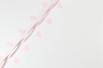 Top view of pink ribbon and pink hearts on white background. Valentine's day, love. Shiny rolled fabric, silk and satin material. Copy space, flat lay.