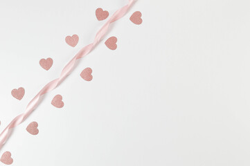 Naklejka premium Top view of pink ribbon and pink glitter hearts on white background. Valentine's day, love. Shiny rolled fabric, silk and satin material. Copy space, flat lay.