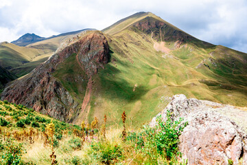 A mountain with a green hillside and a cloudy sky. The mountain is covered in grass and trees