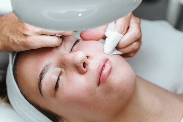 Professional beautician manually removing acne and pimples from young woman's face in a modern equipped beauty spa studio. Beautification and skin health concept.