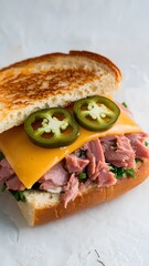 A spicy tuna melt with melted cheddar, spicy mayo, and jalape&ntilde;os, isolated on a white background