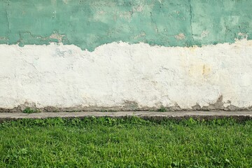 Fototapeta premium Green wall with white paint peeling, contrasting with lush grass in a tranquil outdoor setting