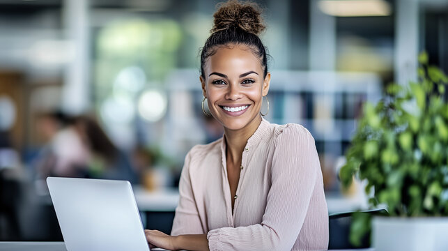Confident Smiling African American, Biracial Businesswoman with Bun in Office, Freelance, Worker, Employee, Looking at Camera, Sitting at Desk with Laptop Computer.