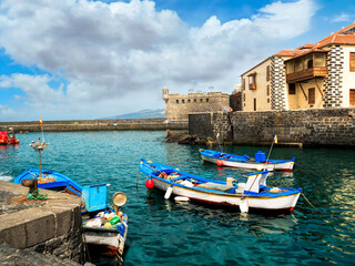 A charming harbor scene in Puerto de la Cruz, Tenerife, featuring colorful fishing boats, turquoise...