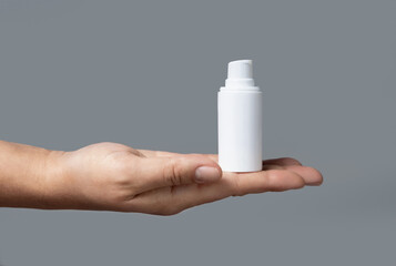 Female hand holding white cosmetic pump bottle against grey close up, mockup, copy space