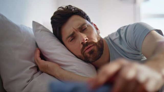 Morning man lying bed waking up closeup. Happy brunette looking mobile phone