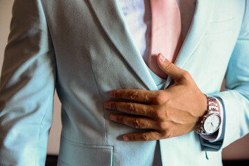 Close-up of a man's hands buttoning a blue jacket over a white shirt and pink tie