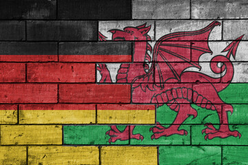 colourful painted big flag of germany and flag of wales on a massive old brick wall background. concept