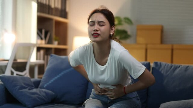 Young woman is experiencing intense abdominal pain. She is writhing in discomfort on a sofa.