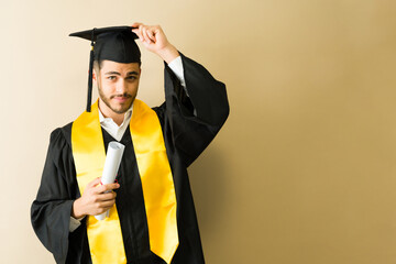 Proud graduate holding diploma and adjusting graduation cap